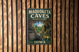 A vintage metal sign for the Maquoketa Caves State Park in Iowa, featuring a scenic illustration of the cave system.
