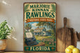 A vintage-style sign for Marjorie Kinnan Rawlings Historic State Park in Florida, featuring a typewriter, a house, and palm trees.