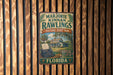 A vintage-style metal sign for Marjorie Kinnan Rawlings Historic State Park in Florida, featuring a typewriter and a house surrounded by palm trees.