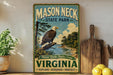 A vintage-style sign for Mason Neck State Park in Virginia, featuring an eagle perched on a tree branch with a scenic landscape in the background.