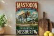 A vintage-style sign for the Mastodon State Historic Site in Missouri, featuring an illustration of a skeleton of a woolly mammoth and a wooden paddle.