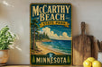 A vintage-style sign for McCarthy Beach State Park in Minnesota, featuring a scenic beach landscape with pine trees and a body of water.