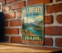 A vintage-style metal sign for McCroskey State Park in Idaho, featuring a scenic mountain landscape and a lake.
