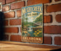 A vintage-style metal sign for McGhee Creek State Park in Oklahoma, featuring a scenic landscape with a waterfall and flowers.