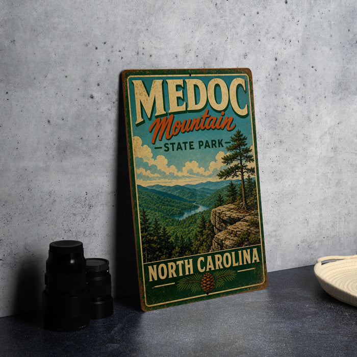 A vintage-style metal sign for Medoc Mountain State Park in North Carolina, featuring a scenic mountain landscape with pine trees and a river.