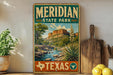 A vintage-style metal sign for Meridian State Park in Texas, featuring a scenic landscape with a mountain, river, and desert vegetation.