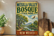A vintage-style sign for Mesilla Valley Bosque State Park in New Mexico, featuring a scenic landscape with a river, mountains, and a bird in flight.