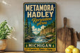 A vintage-style metal sign for Metamora-Hadley Recreation Area in Michigan, featuring a scenic landscape with a waterfall and pine trees.