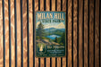 A vintage metal sign for Milan Hill State Park, featuring a scenic landscape with a lake and mountains.