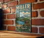 A vintage-style metal sign for Miller State Park, featuring a scenic landscape with mountains, trees, and a lake.