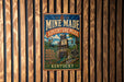 A vintage-style metal sign for the Mine Made Adventure Park in Kentucky, featuring a colorful illustration of the park's attractions and a sign that says "Real Fun in a Real Mine".