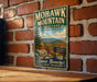 A vintage-style metal sign for Mohawk Mountain State Park in Connecticut, featuring a scenic mountain landscape with autumn foliage.