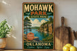 A vintage-style metal sign for Mohawk Park, Oklahoma, featuring a scenic landscape with a lake and mountains.