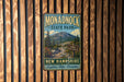 A vintage metal sign for Monadnock State Park, featuring a mountain landscape and trail signs, is displayed on a wooden wall.