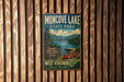 A vintage metal sign for Moncover Lake State Park, featuring a scenic image of a lake surrounded by mountains and a red canoe, is displayed on a wooden wall.