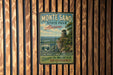 A vintage metal sign for Monte Sano State Park in Alabama, featuring a scenic image of a mountain and a lighthouse, mounted on a wooden wall.