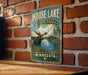 A vintage-style metal sign for Moose Lake State Park in Minnesota, featuring a moose in a grassy field with a lake in the background.