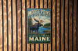 A vintage metal sign for Moose Point State Park, featuring a moose in a scenic landscape with a river and pine trees.