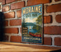 A vintage-style metal sign for Moraine State Park in Pennsylvania, featuring a scenic image of a lake, mountains, and a canoe.