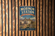 A vintage-style metal sign for Mormon Station, a historic park in Nevada, featuring an illustration of a wagon and a sign that says "A reminder of our Pioneer Heritage".