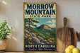 a vintage-style metal sign for Morrow Mountain State Park, with a scenic mountain landscape and pine trees. The sign is displayed on a wooden shelf, surrounded by various kitchen utensils and a potted plant.