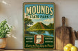A vintage-style sign for Mounds State Park, featuring a scenic landscape with a hill, trees, and a lake. The sign also includes the words "Indiana", "History", "Nature", "Heritage", and "Adventure", suggesting the park offers various outdoor activities and attractions.