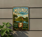 A vintage metal sign for Mounds State Park, featuring a landscape with a hill, trees, and a lake, mounted on a gray wall.