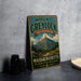 A vintage metal sign for Mount Greylock State Reserve in Massachusetts, featuring a mountain landscape and the text "The Highest Peak in Massachusetts".