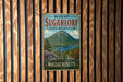 A vintage metal sign for Mount Sugarloaf State Reserve in Massachusetts, featuring a scenic mountain landscape with a lake and pine trees.