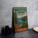 A vintage-style metal sign for Mouttail Landing State Park in Tennessee, featuring a scenic landscape with a lake, bridge, and mountains.