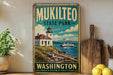 A vintage-style metal sign for Mukilteo State Park in Washington, featuring a lighthouse and a mountain backdrop.