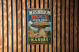 A vintage metal sign for Mushroom Rock State Park in Kansas, featuring a large mushroom formation and the text "Mushroom Rock State Park Kansas Discover the Un expected".