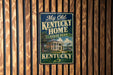 A vintage-style sign for Kentucky State Park hangs on a wooden wall, featuring a house and trees in the background.