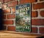A vintage-style sign for Kentucky State Park hangs on a brick wall, featuring an illustration of a stately building and a river.