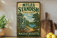 A vintage-style sign for Myles Standish State Forest in Massachusetts, featuring a scenic landscape with pine trees, a lake, and a path leading through the forest.