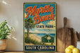 A vintage-style metal sign for Myrtle Beach State Park in South Carolina, featuring a palm tree and beach scene, is displayed on a shelf next to a wooden cutting board and some lemons.