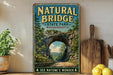 A vintage-style metal sign for "Natural Bridge State Park, Massachusetts" featuring a scenic image of a stone arch surrounded by trees and a winding road.