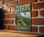 A vintage-style metal sign for Nelson-Kennedy Lidges State Park in Ohio, featuring a scenic image of the park's natural landscape.