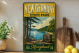 A vintage-style metal sign for New Germany State Park, featuring a scenic landscape with a lake and pine trees, is displayed on a shelf next to a wooden cutting board and some lemons.