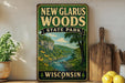 A vintage-style sign for New Glarus Woods State Park in Wisconsin, featuring a scenic landscape with a river, trees, and mountains.