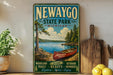 A vintage-style metal sign for Newaygo State Park in Michigan, featuring a scenic image of a canoe on a lake surrounded by pine trees.
