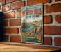 A vintage metal sign welcoming visitors to Newton Hills State Park in South Dakota, featuring a scenic landscape with a river and mountains.