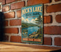 A vintage-style metal sign for Nick's Lake State Park in New York, featuring a scenic landscape with a lake, mountains, and pine trees.