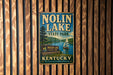A vintage metal sign for Nolin Lake State Park in Kentucky, featuring a scenic image of the lake and a sailboat.
