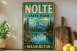 A vintage-style sign for Nolte State Park in Washington, featuring a scenic mountain landscape with a lake and pine trees.