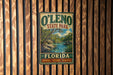 A vintage-style sign for O'Leno State Park in Florida, featuring a scenic landscape with a river and palm trees.