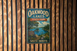 A vintage-style metal sign for Oakwood Lakes State Park in South Dakota, featuring a scenic landscape with a lake, trees, and mountains.