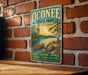 A vintage-style metal sign for Oconee State Park in South Carolina, featuring a scenic illustration of a lake, trees, and a red canoe.