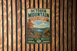 A vintage metal sign for October Mountain State Forest in Massachusetts, featuring a scenic landscape with mountains, trees, and a river.