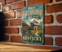 A vintage-style metal sign for Old Fort Harrod State Park in Kentucky, featuring an illustration of a wooden fort with a flag and a path leading to the entrance.